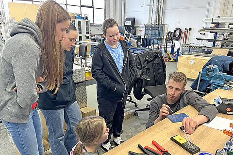 An employee explains a component in production to the four girls.